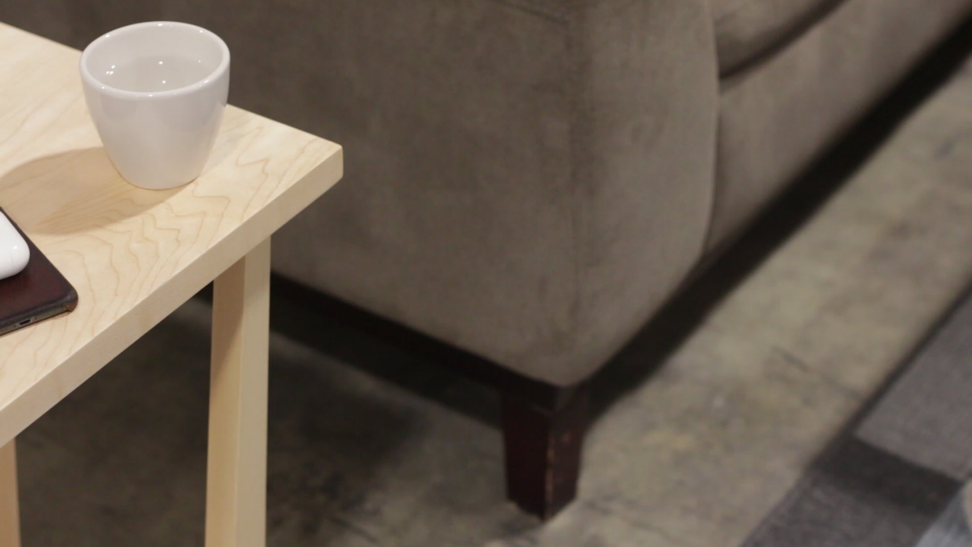 A side table placed in a living room with a plant and coffee mug sat on the table top. The side table is made from light maple hardwood and is crafted in Scandinavian minimalist modern design.