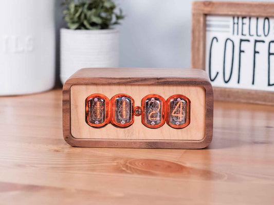 Clock sits on counter table made from solid walnut with a contrasting maple face. The design uses retro Nixie tubes for a warm orange glow.