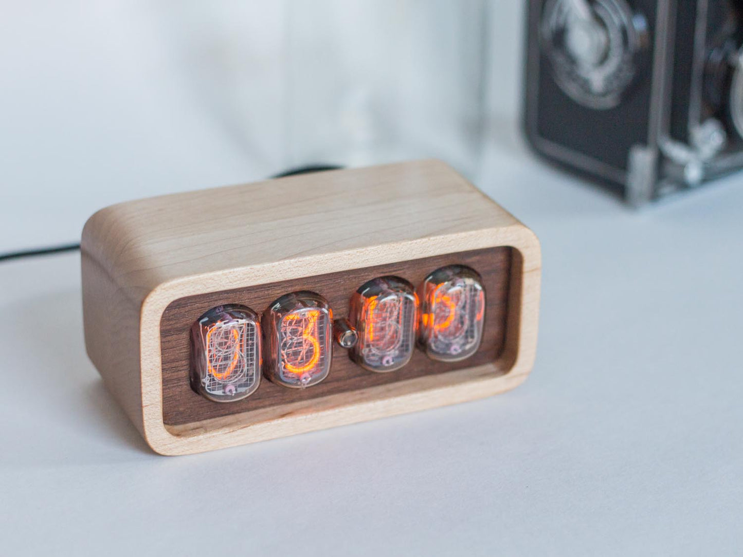Clock sits on counter table made from solid maplewith a contrasting walnut face. The design uses retro Nixie tubes for a warm orange glow.