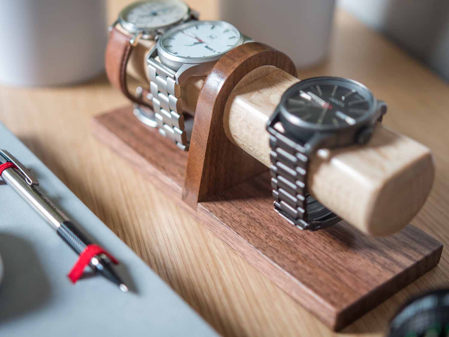 Watch display holder rests on a table, made of a long, wooden block base with one round dowel sticking out horizontally, enough space to hold four watches.