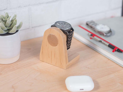 One watch rests on a smooth maple dowel which rests on a strong maple base. Set on a desk with notebook and camera. The warm wood contrasts nicely with the mechanical metal watch.