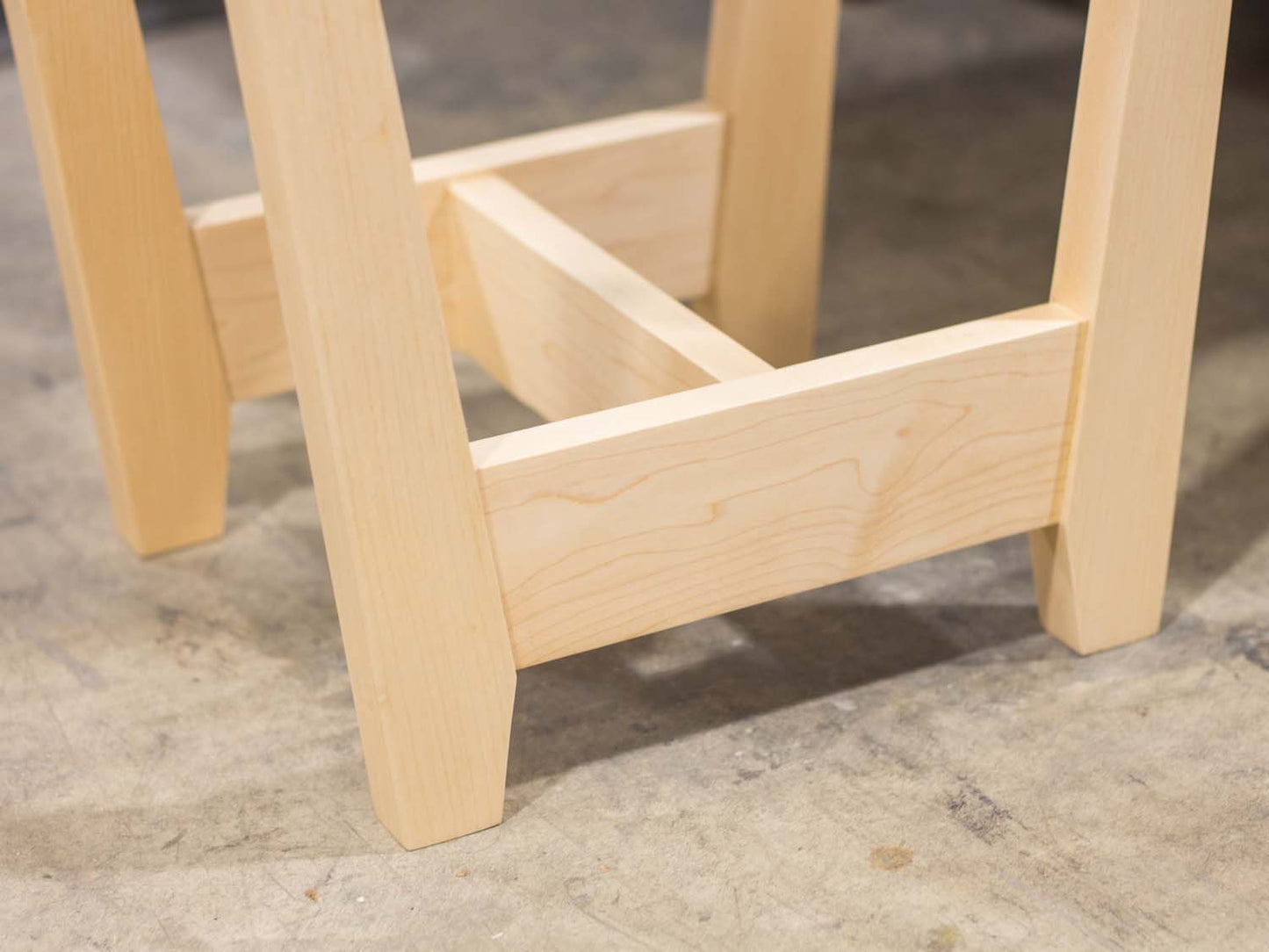 A side table placed in a living room with a plant and coffee mug sat on the table top. The side table is made from light maple hardwood and is crafted in Scandinavian minimalist modern design.