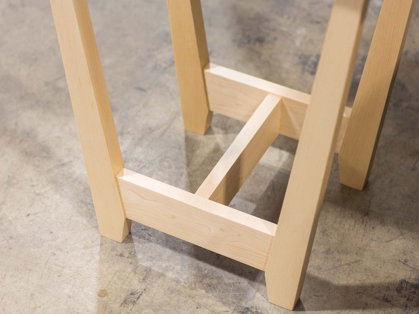 A side table placed in a living room with a plant and coffee mug sat on the table top. The side table is made from light maple hardwood and is crafted in Scandinavian minimalist modern design.